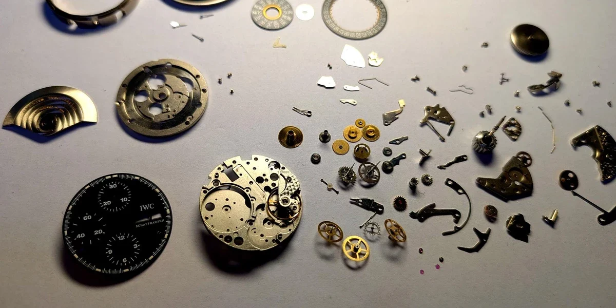 Rozebrany zegarek IWC Schaffhausen – mechanizm zegarka i drobne części ułożone na stole podczas serwisu
